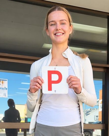 A smiling young woman holds up her red P plate